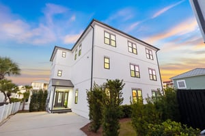 Modern white vacation home with spacious threestory design and stunning sunset backdrop in a palmlined neighborhood.