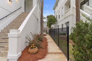 Elegant white building entrance featuring charming landscaping with mulched garden beds and mature palm trees in a peaceful residential setting.