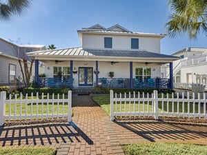 Charming coastal home with turquoise accents and welcoming front porch surrounded by tropical palms and picket fence.
