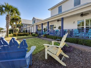 Charming coastal property with vibrant blue railings, tropical palms, and relaxing Adirondack chairs set among manicured gardens.