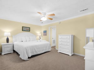 Drift off peacefully in this spacious bedroom featuring a plush king bed, ceiling fan, and coastal artwork that sets a serene mood.
