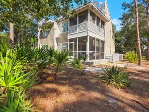 A charming beach cottage nestled among mature trees and tropical palms, featuring a screened porch