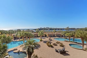Spacious pool area featuring multiple swimming pools, hot tubs, and lush tropical landscaping with coastal views beyond.