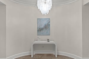 Your elegant foyer welcomes you with a stunning crystal chandelier casting warm light over a sleek console table beneath beautiful artwork.