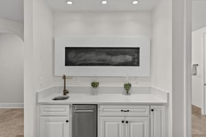 Your private wet bar awaits with elegant white cabinetry, pristine countertops, and stylish artwork—perfect for evening cocktails or morning coffee.