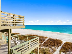 Elevated wooden deck with beach access overlooks pristine white sand and turquoise waters under endless blue sky.