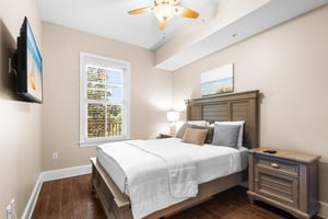 Rest peacefully in this queen size bedroom with crisp linens, warm wood furnishings, and gentle natural light streaming through the window.