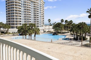 Modern beachfront resort with sparkling pool surrounded by tropical palms and ocean views.