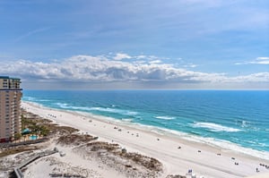 Aerial view of pristine beachfront with white sand and turquoise waters stretching to the horizon.