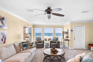 Your beachfront living room captures endless Gulf views through floortoceiling windows, where gentle ceiling fan breezes complement the coastal décor.