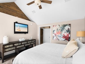 Drift into coastal dreams in the serene primary bedroom, featuring a plush king bed, tropical artwork, and rustic wood accents that create the perfect retreat.