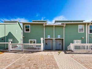 Unique townhome complex with charming green siding and white trim under brilliant blue skies.