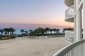 Breathtaking oceanfront balcony with panoramic sea views and stunning sunset skies over swaying palm trees.