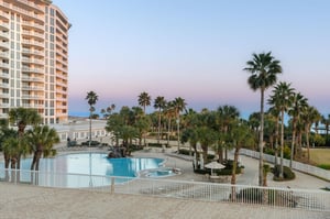 Elegant resort towers rise above tropical palms surrounding a pristine pool deck at twilight.