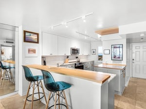 The modern kitchen features sleek white cabinets, warm wood countertops, and stylish turquoise bar seating