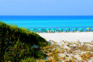 Pristine beach with white sand and turquoise waters, dotted with green umbrellas and beach chairs for perfect relaxation.