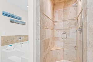 Unwind in your luxurious marble bathroom featuring a rainfall shower and soaking tub, where coastal artwork adds peaceful touches to your private retreat.