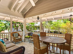 Relax on your spacious covered porch with wicker dining table and cozy seating, surrounded by lush greenery.