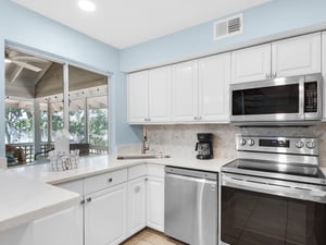 Your fully equipped kitchen features stainless steel appliances and white cabinetry, with serene views of greenery through the window.