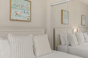 Sink into crisp white linens in your serene bedroom, where coastal artwork adds gentle splashes of color to your peaceful retreat.