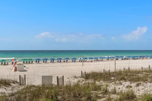 Pristine white sand beach with turquoise waters and colorful umbrellas stretching along the coastline under clear blue skies.