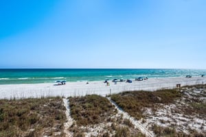 Pristine white sand beach with turquoise waters stretches endlessly under brilliant blue skies, where beachgoers relax beneath colorful umbrellas.