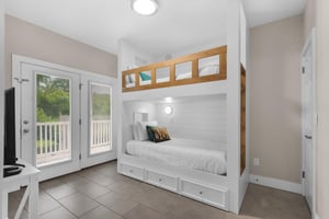 Bedroom 3 1st Fl features custom white shiplap beds with cozy storage drawers, natural light streaming through doors to the deck, and all the restful charm you need after a beach day.