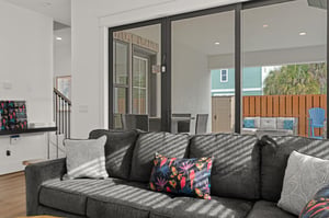 Sink into plush seating while natural light streams through expansive glass doors connecting your living space to a private patio  pool area complete with outdoor furniture and lush tropical greenery