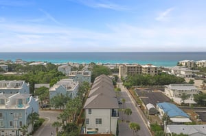 Elevated perspective showcasing a coastal community with beach access. The property is situated among treelined streets and residential homes, just moments from pristine turquoise waters.