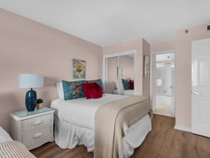 Your serene bedroom retreat features soft pink walls, plush bedding with vibrant floral pillows, and convenient access to your private ensuite bathroom.