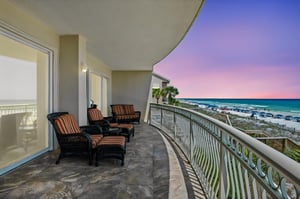 Spacious beachfront balcony with comfortable seating overlooking white sand and turquoise waters, perfect for sunset cocktails after a beach day.