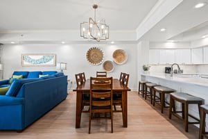 The openconcept living space flows seamlessly from plush blue sofas to a warm wooden dining table and sleek white kitchen, perfect for gathering.