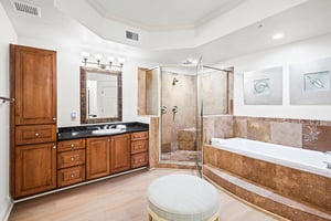 The primary bathroom offers a deep soaking tub, spacious walkin shower with dual showerheads, elegant stone tile, and abundant storage in rich wood cabinetry.