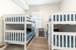 Perfect for families or groups, this bright room features two white bunk beds with deep teal linens, offering cozy sleeping space for kids or friends traveling together.
