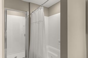 A modern bathroom featuring a spacious tub with crisp white curtain and a separate glassenclosed shower.