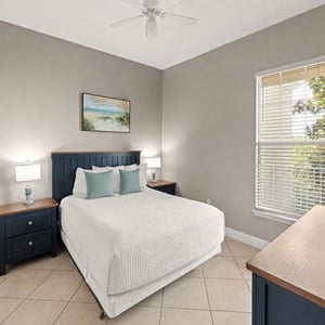 Guest bedroom features crisp linens and coastal charm, with natural light streaming through the window to brighten your peaceful retreat after a day of adventure.