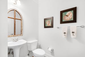 The powder room features coastal accents, soft lighting, and a charming arched mirror.