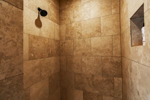 Shower nook with cream tile, and black shower head.
