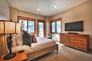 Fourth bedroom with king bed, upholstered bedframe and headboard, wooden dresser, wall mounted TV and glass door to a patio.