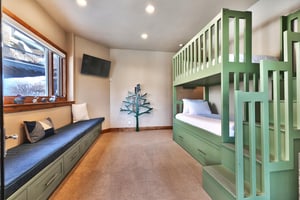 The bedroom has green twin bunk beds plus a trundle, wall mounted TV, built in window seat, and tree bookcase.