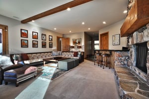 Second living room with a wooden wet bar and black countertop, spacious sectional, and wooden coffee table, and gallery wall.