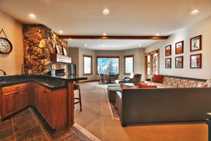 Medium toned wooden wet bar with a black countertop and bar seating, located in the second living room.
