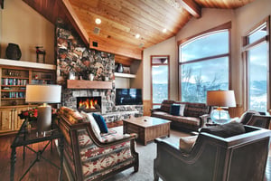 The living room has a wood burning fireplace with floor to ceiling stone surround, Smart TV, 2 couches, and 2 club chairs.