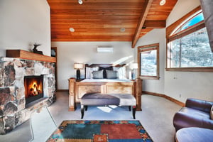 Four poster wooden king bed with grey upholstered bench at the end, a flagstone fireplace hearth and western inspired rug.