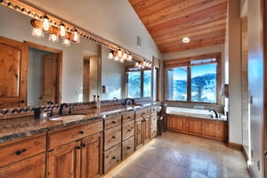 Ensuite bathroom with long dual sink vanity and mirror, granite countertops and three vanity lights, next to a soaker tub.