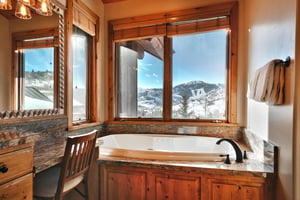 Jetted soaking tub with granite rim next to a window with views of Bald Mountain covered in snow and evergreen trees.