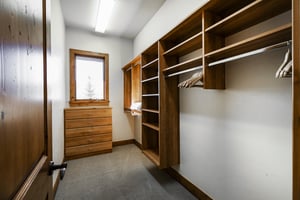 Spacious walk in closet off the first bedroom with built in shelves and hanger rods, wooden dresser, and window.