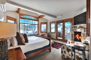 Second bedroom suite with king bed, many windows framing snowy mountains, gas fireplace, and two cowboy print accent chairs