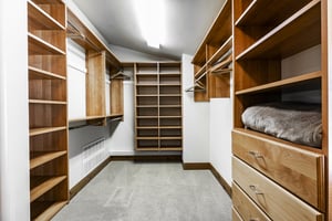 Walk in closet with builtin wooden storage cubbies, drawers, hanging rods, bright lighting and white walls.