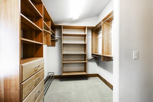 Walk in closet with builtin wooden storage cubbies, drawers, hanging rods, bright lighting and white walls.